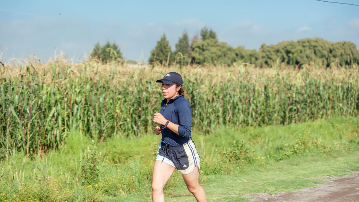 Woman jogging along a rural path next to a cornfield, enjoying fitness in nature.